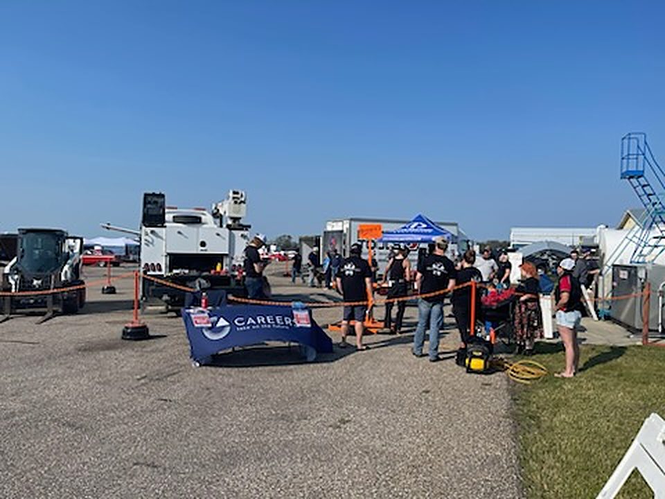 Spectators along the fence line at the competition grounds with a CAREERS banner and heavy equipment in the background